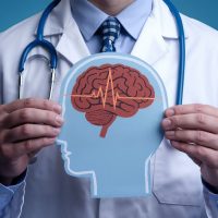 A doctor holding a paper cutout of human head with brain with electric currents. epilepsy, migraine seizure disorder, neurological disorder, migraines, brain waves, mental health concept.