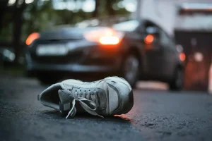 A solitary sneaker lies on a dimly lit asphalt road, with a car in the background, its headlights glowing softly. The scene feels tense and foreboding.