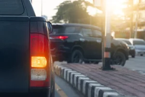 A black pickup truck with its brake light on is in traffic, next to a curb, under a warm sunset glow. Other vehicles are visible on the road.