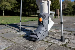 person walking outdoors with crutches and an orthopedic cam walker boot during leg injury rehabilitation